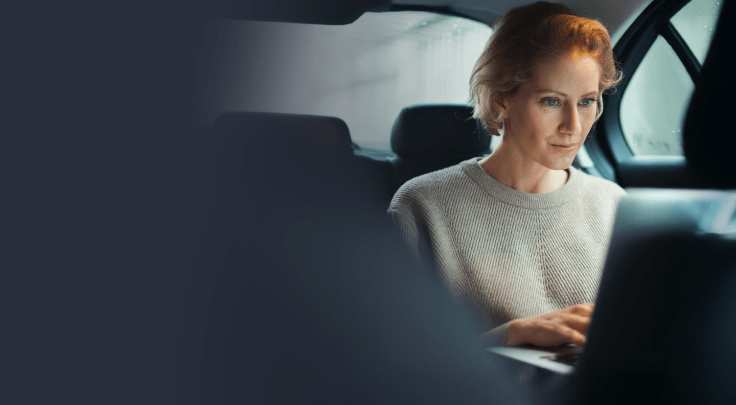 Woman in the back of a car, looking at a laptop